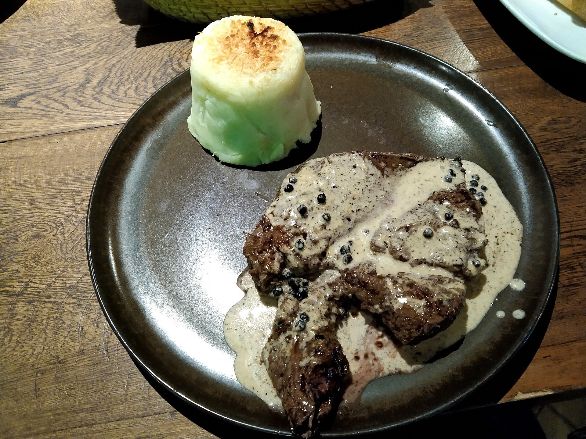A plate of pepper steak topped with cognac sauce, topped with mashed potatoes with mozzarella cheese gratin (Papi Steak)